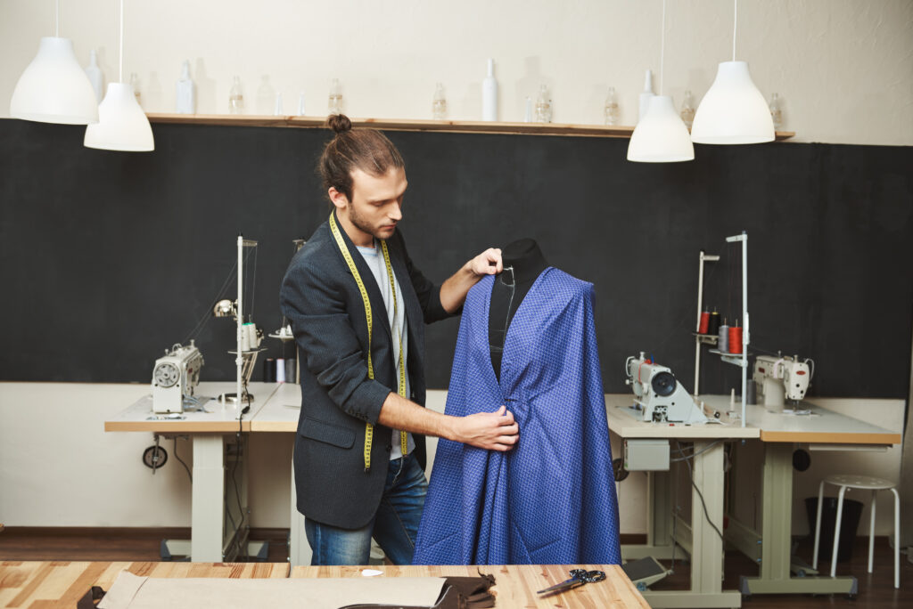 young shaved good looking caucasian male fashion designer stylish outfit working new blue dress spring collection his workshop artist creating beautiful clothes his workshop